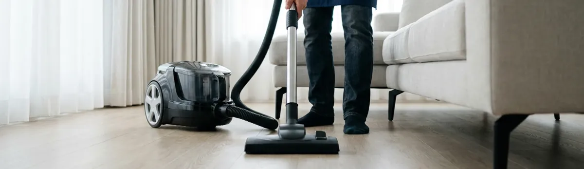 Professional house cleaner vacuuming a living room floor with a canister vacuum cleaner, Atlanta, GA.