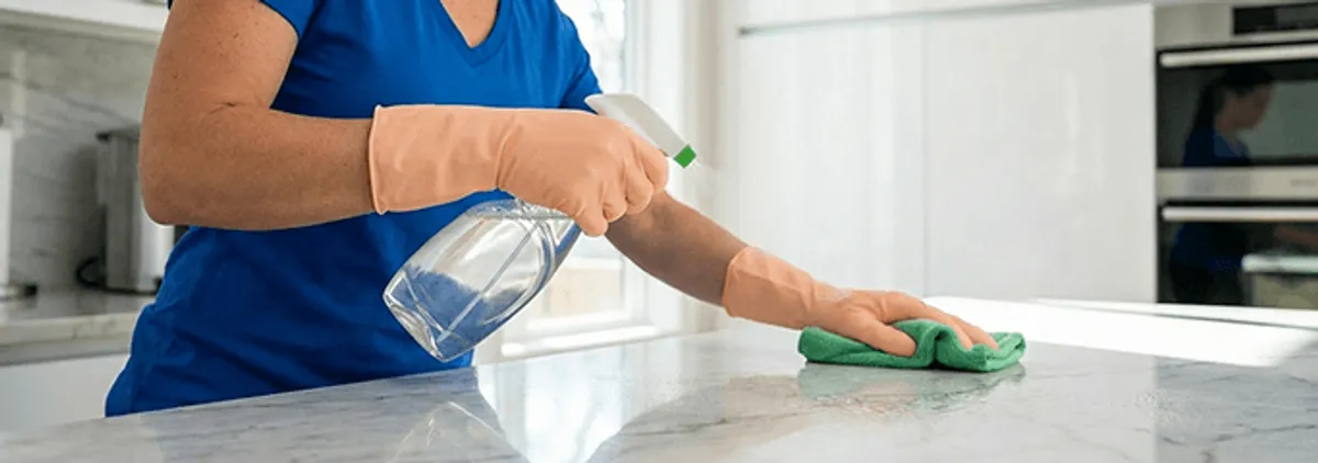 Maid service worker spraying and wiping a kitchen countertop with a microfiber cloth for sanitizing, Atlanta, GA.